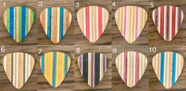 Puede incluir: Diez p&uacute;as de guitarra de madera con rayas verticales en varios colores, incluyendo azul, verde, naranja, rojo, morado y amarillo. Cada p&uacute;a tiene un patr&oacute;n de rayas &uacute;nico, mostrando una variedad de tonos de madera.
