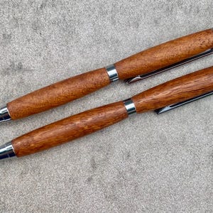 Peut inclure: Deux stylos à bille dotés de corps en bois poli avec un motif de grain distinct. Chaque stylo comprend une pointe en métal argenté, une bague centrale, un clip de poche et un mécanisme à bouton-poussoir au sommet, au design élégant et fonctionnel.