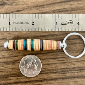 May include: A wooden keychain with a multi-colored striped design and a silver key ring. The keychain is about 2 inches long and is made from recycled skateboard wood.