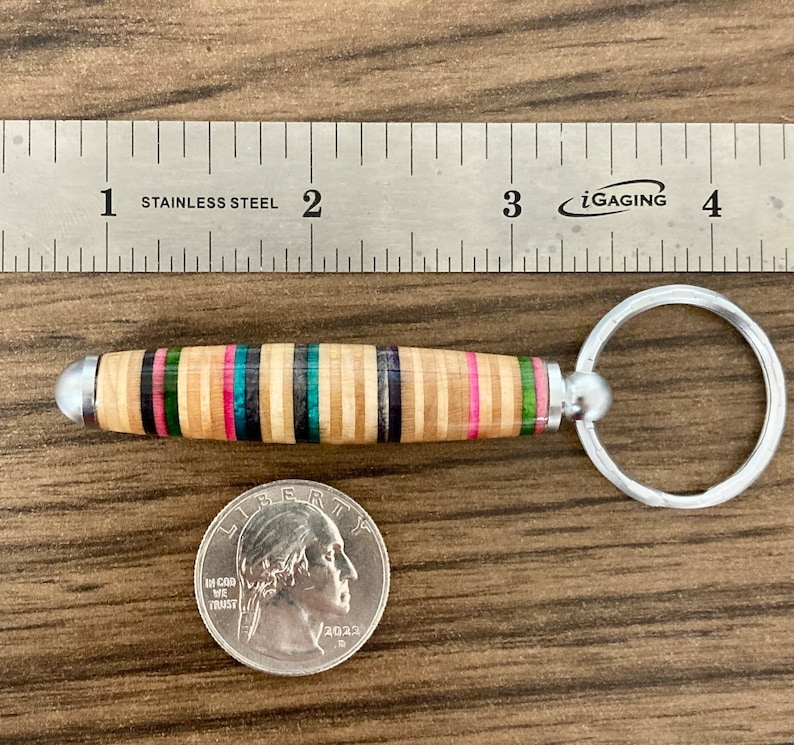 May include: A wooden keychain with a multi-colored striped design and a silver key ring. The keychain is about 2 inches long and is made from recycled skateboard wood.