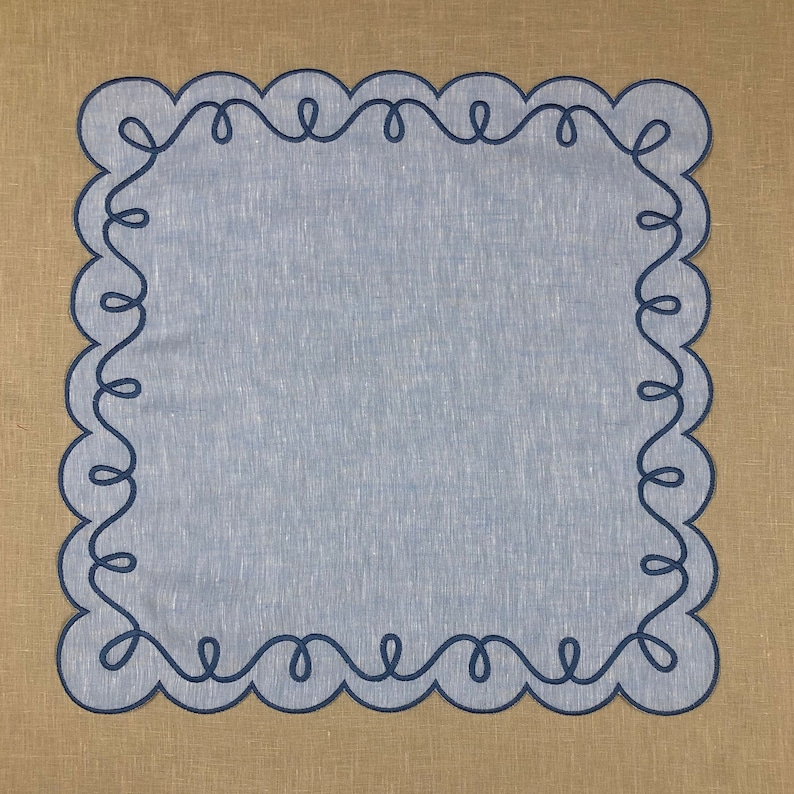 May include: A light blue linen placemat with a scalloped edge and a dark blue embroidered design.