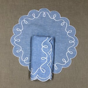 May include: A blue linen placemat with a white scalloped edge and a matching blue linen napkin with a white scalloped edge.