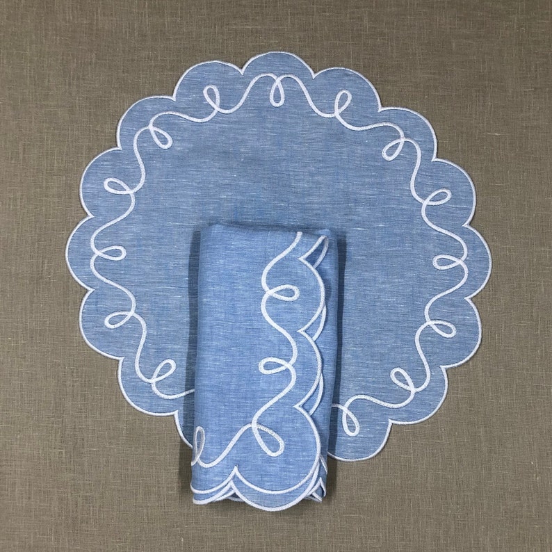 May include: A blue linen placemat with a white scalloped edge and a matching blue linen napkin with a white scalloped edge.