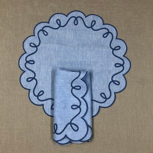 May include: Blue linen placemat with a scalloped edge and a matching blue linen napkin. Both have a dark blue embroidered design.