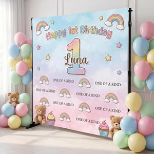 May include: A backdrop for a first birthday celebration, featuring a pastel color scheme with balloons, teddy bears, and the text "Happy 1st Birthday Luna." The design includes rainbows, stars, and cupcakes, with the phrase "ONE OF A KIND."