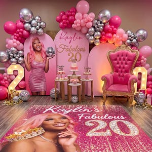 May include: A pink and silver 20th birthday party setup. The decor includes a pink throne chair, balloon arches, a photo backdrop, and a floor mat with the birthday girl's image and the words "Kaylin's Fabulous 20."