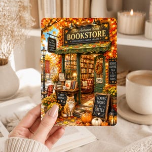 May include: A rectangular print depicting an autumn-themed bookstore storefront with orange foliage, a ginger cat sitting on the sidewalk, pumpkins, and signs reading The Autumn Leaf BOOKSTORE, NEW ARRIVALS, and LEAVES BOOKS & LATTES.