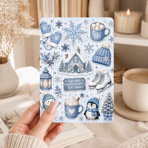 May include: A sticker sheet featuring winter-themed illustrations in shades of blue and white, including a house, mugs of cocoa, a penguin, a snowman, ice skates, mittens, a beanie, snowflakes, and a sign that reads COZY DAYS WARM HEARTS SOFT SNOW.