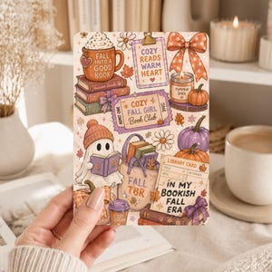 Può includere: Un adesivo rettangolare con illustrazioni a tema autunnale che includono un fantasma che legge, pile di libri, zucche, una borsa, una candela e una tazza. Il testo include "Fall into a good book", "Cozy reads warm heart", "Cozy fall girl book club", "Fall TBR" e "In my bookish fall era".