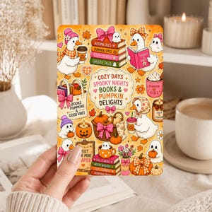 May include: A rectangular sticker featuring white ducks, ghosts, pumpkins, and stacks of books with pink bows. The text reads COZY DAYS SPOOKY NIGHTS BOOKS & PUMPKIN DELIGHTS, BOOKS PUMPKINS & GOOD VIBES, JUST ONE MORE CHAPTER, and various book titles in orange, pink, and green.