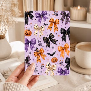 May include: A rectangular card featuring a repeating pattern on a light purple background. The design includes various bows in black, orange, purple, and cream, interspersed with small orange pumpkins, black bats, spider webs, and stars.