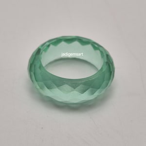 Könnte beinhalten: Ein facettierter, hellgrüner Ring. Der Ring hat ein geometrisches Design mit mehreren Facetten, das einen funkelnden Effekt erzeugt. Der Text "jadigemsart" ist auf dem Ring sichtbar. Der Ring ist ein massives Band, wahrscheinlich aus Glas oder einem ähnlichen Material.