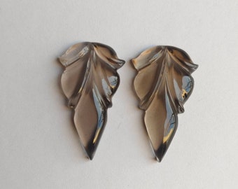 May include: Two smoky quartz leaf-shaped pendants. Each pendant has detailed veining and a polished, glossy finish. The leaves are a translucent, brownish-gray color, with a pointed tip and a curved top.