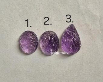 Könnte beinhalten: Drei geschnitzte Amethyst-Edelsteine in ovaler und tropfenförmiger Form. Jeder Edelstein weist komplizierte Blumen- und Wirbelmuster auf. Die Edelsteine sind mit 1, 2 und 3 nummeriert. Der Hintergrund ist hellgrau.