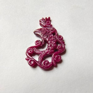 May include: A carved ruby pendant in the shape of a fish with intricate details. The pendant is a deep red color and has a glossy finish.