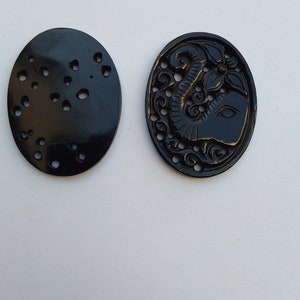 May include: Two black oval-shaped carved buttons. One button has a detailed carving of an elephant with a flower. The other button has a pattern of small circles.