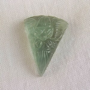 May include: A carved green gemstone pendant in the shape of a triangle with a floral design.