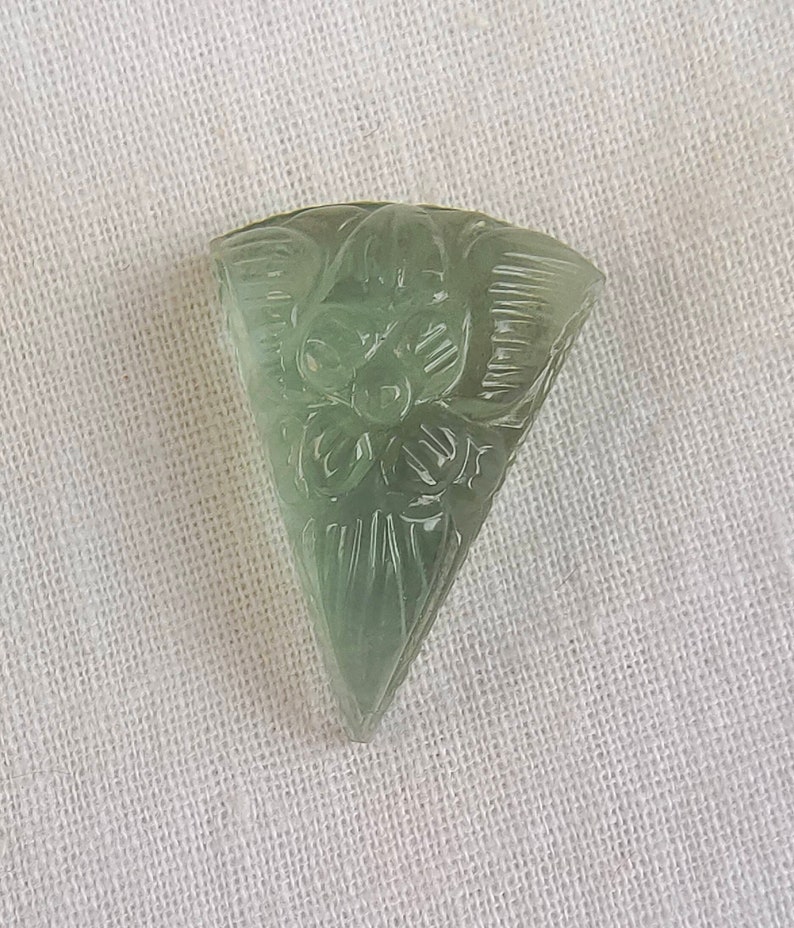 May include: A carved green gemstone pendant in the shape of a triangle with a floral design.