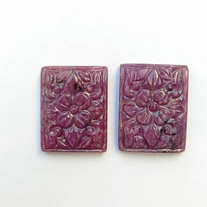 May include: Two carved pink ruby gemstones with a floral design. The gemstones are rectangular in shape and have a polished finish.