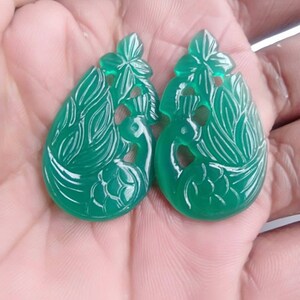 Peut inclure: Deux paons en jade vert sculptés dans un design détaillé. Les paons sont face à face et ont un motif de fleur sur la tête.