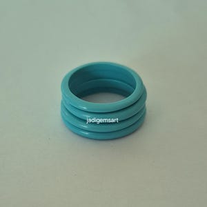 Op de afbeelding: Een stapel van vier turquoise ringen. De ringen hebben een effen, levendige blauwgroene kleur. De ringen zijn op elkaar gestapeld, waardoor een gelaagd effect ontstaat. De ringen zijn glad en glanzend. De tekst "jadigemsart" is zichtbaar.