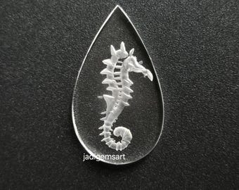 Puede incluir: Colgante transparente en forma de lágrima con un grabado detallado de un caballito de mar. El caballito de mar está grabado en el centro del colgante, mostrando sus intrincados detalles. El texto "jadigemsart" está impreso en la parte inferior del colgante.