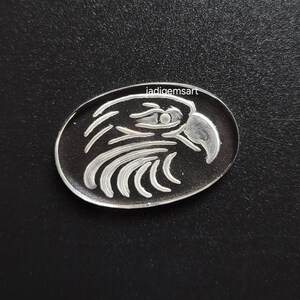 May include: Oval-shaped silver pendant with an engraved eagle design. The eagle's head is depicted in profile, with detailed feathers and a sharp beak. The text "iadigemsart" is printed on the top of the pendant. The pendant is set against a black background.