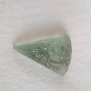 May include: A carved green gemstone pendant in the shape of a triangle with a floral design.
