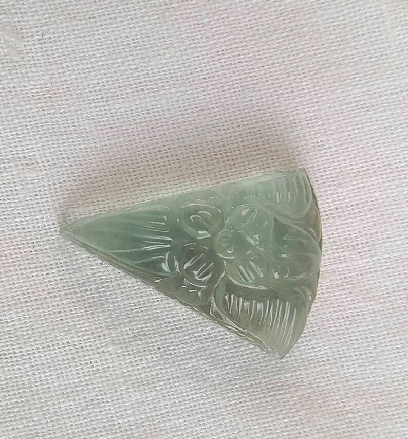 May include: A carved green gemstone pendant in the shape of a triangle with a floral design.