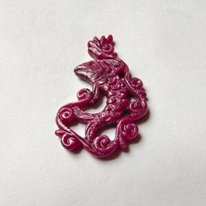May include: A carved ruby pendant in the shape of a mythical creature with intricate details. The pendant is a deep red color and has a glossy finish.