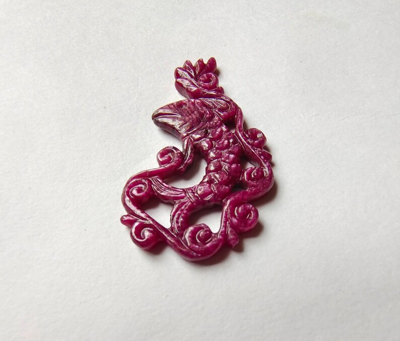 May include: A carved ruby pendant in the shape of a mythical creature with intricate details. The pendant is a deep red color and has a glossy finish.