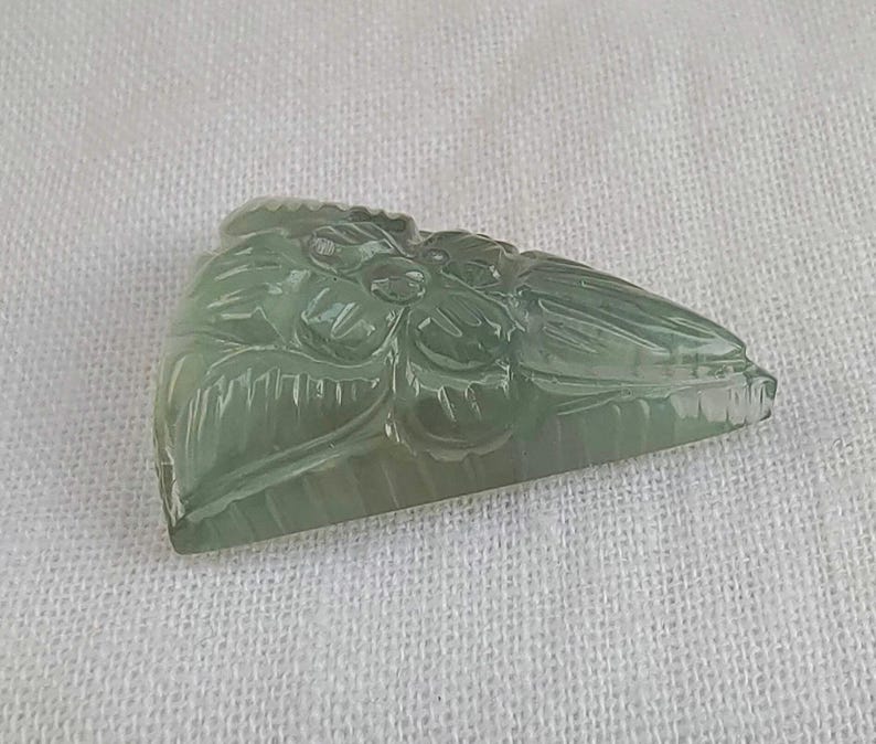 May include: A carved green jade pendant featuring a floral design. The pendant is triangular in shape and has a smooth, polished surface.