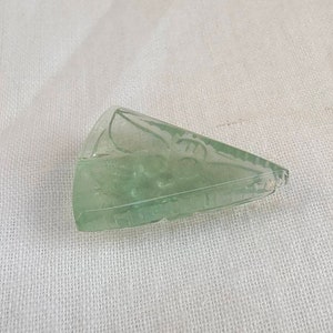 May include: A light green, carved, triangular piece of crystal.