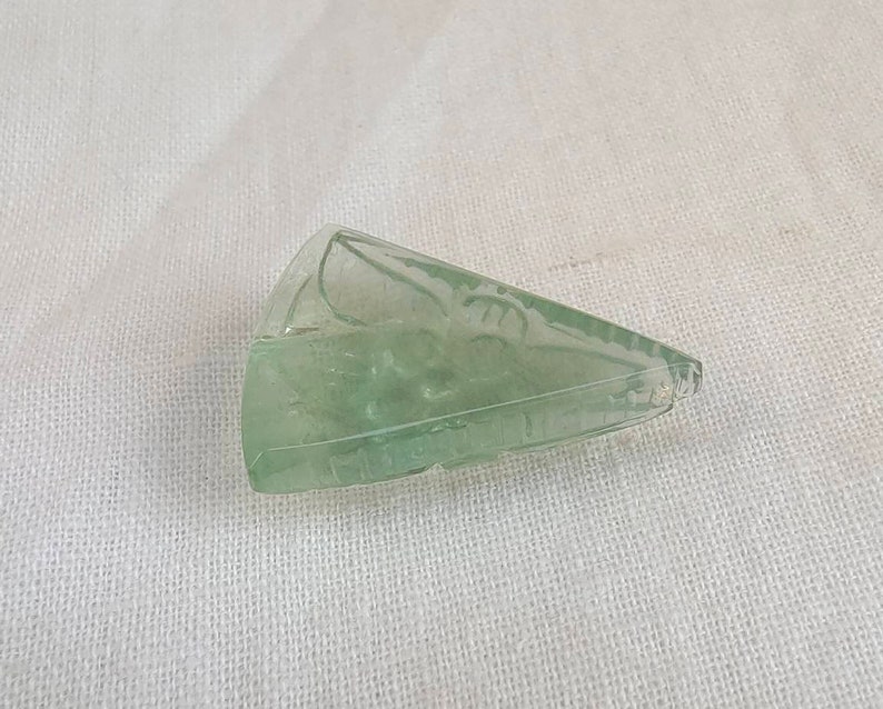 May include: A light green, carved, triangular piece of crystal.