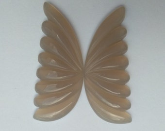 May include: A pair of carved agate wings in a light brown color. The wings are symmetrical and have a delicate, fan-like design.