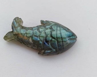 Puede incluir: Una piedra preciosa de labradorita verde y azul tallada en forma de pez. El pez tiene un diseño detallado y un brillo iridiscente.