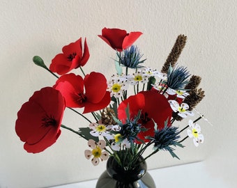 Puede incluir: Un ramo de amapolas rojas y flores silvestres blancas dispuestas en un jarrón negro.
