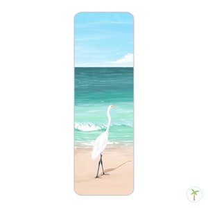 A thick laminated bookmark featuring an illustration print of a Great Egret on the beach, the perfect bookmark for your next beach read