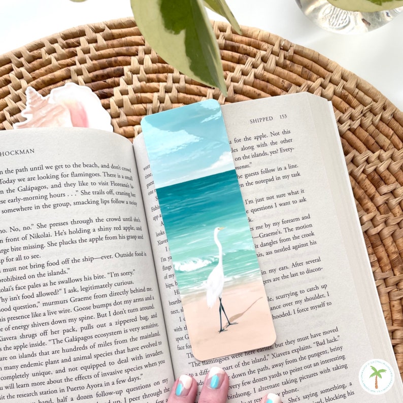 A thick laminated bookmark featuring an illustration print of a Great Egret on the beach, the perfect bookmark for your next beach read