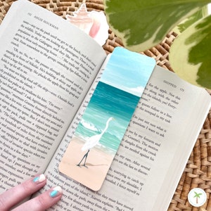 A thick laminated bookmark featuring an illustration print of a Great Egret on the beach, the perfect bookmark for your next beach read
