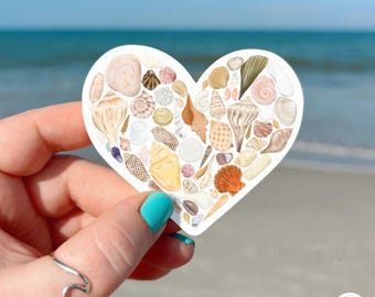 Puede incluir: Una pegatina en forma de corazón con un collage de varias conchas marinas en tonos blanco, beige, marrón y naranja. Las conchas están dispuestas formando una silueta de corazón, mostrando diversas texturas y patrones espirales.