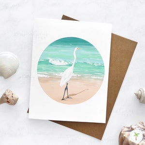 An A2 sized greeting card that features a spot illustration of a Great Egret on the beach near the shoreline