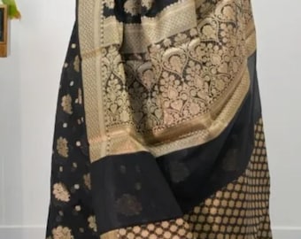 May include: A black saree with gold floral and geometric patterns. The saree features a gold border and intricate detailing. The fabric drapes elegantly, showcasing the rich texture and design. The saree is a traditional garment.
