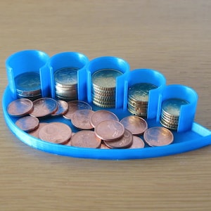May include: A blue plastic coin holder with six compartments. The holder is shaped like a leaf and has a rounded edge. The compartments are filled with stacks of euro coins.