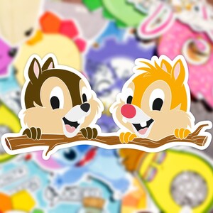 May include: Two cartoon chipmunks, one brown and one orange, are smiling and looking at each other. They are perched on a brown branch, with their paws resting on the branch. The chipmunks are against a background of colourful stickers.