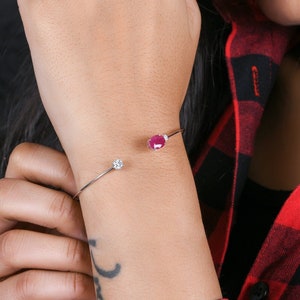 Può includere: Un braccialetto d'argento con una piccola pietra rosa e una pietra trasparente. Il braccialetto è al polso.