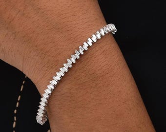 Op de afbeelding: Een zilveren armband met een rij rechthoekige, heldere stenen. De armband wordt om een pols gedragen, tegen een zwarte top.
