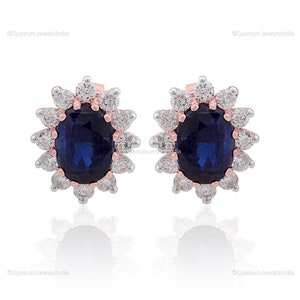 Puede incluir: Un par de pendientes con una piedra preciosa de zafiro ovalada azul rodeada por un halo de diamantes blancos m&aacute;s peque&ntilde;os. Los pendientes est&aacute;n engastados en oro rosa.