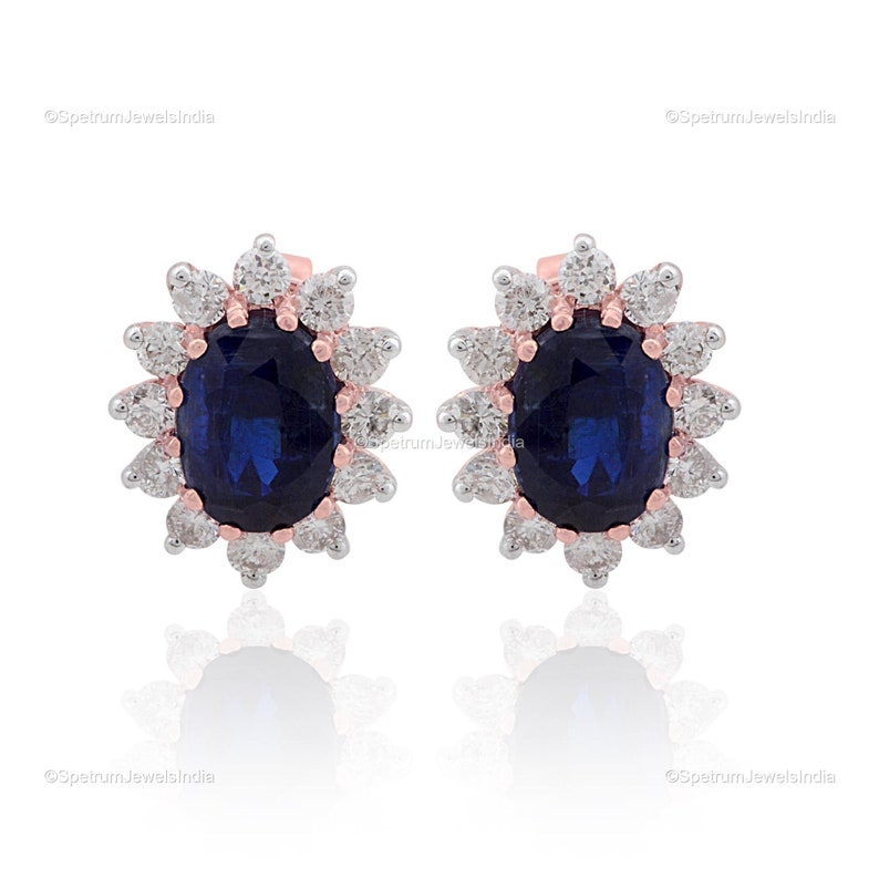 Puede incluir: Un par de pendientes con una piedra preciosa de zafiro ovalada azul rodeada por un halo de diamantes blancos m&aacute;s peque&ntilde;os. Los pendientes est&aacute;n engastados en oro rosa.