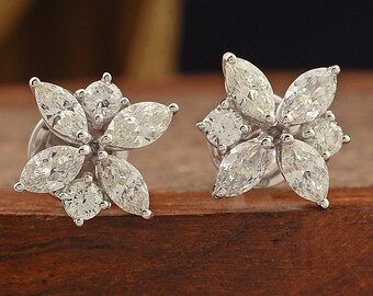 Op de afbeelding: Een paar diamanten oorstekers. Elke oorbel heeft een bloemenontwerp met marquise-geslepen en ronde diamanten, gezet in een zilverkleurig metaal. De oorbellen worden gepresenteerd op een houten oppervlak.